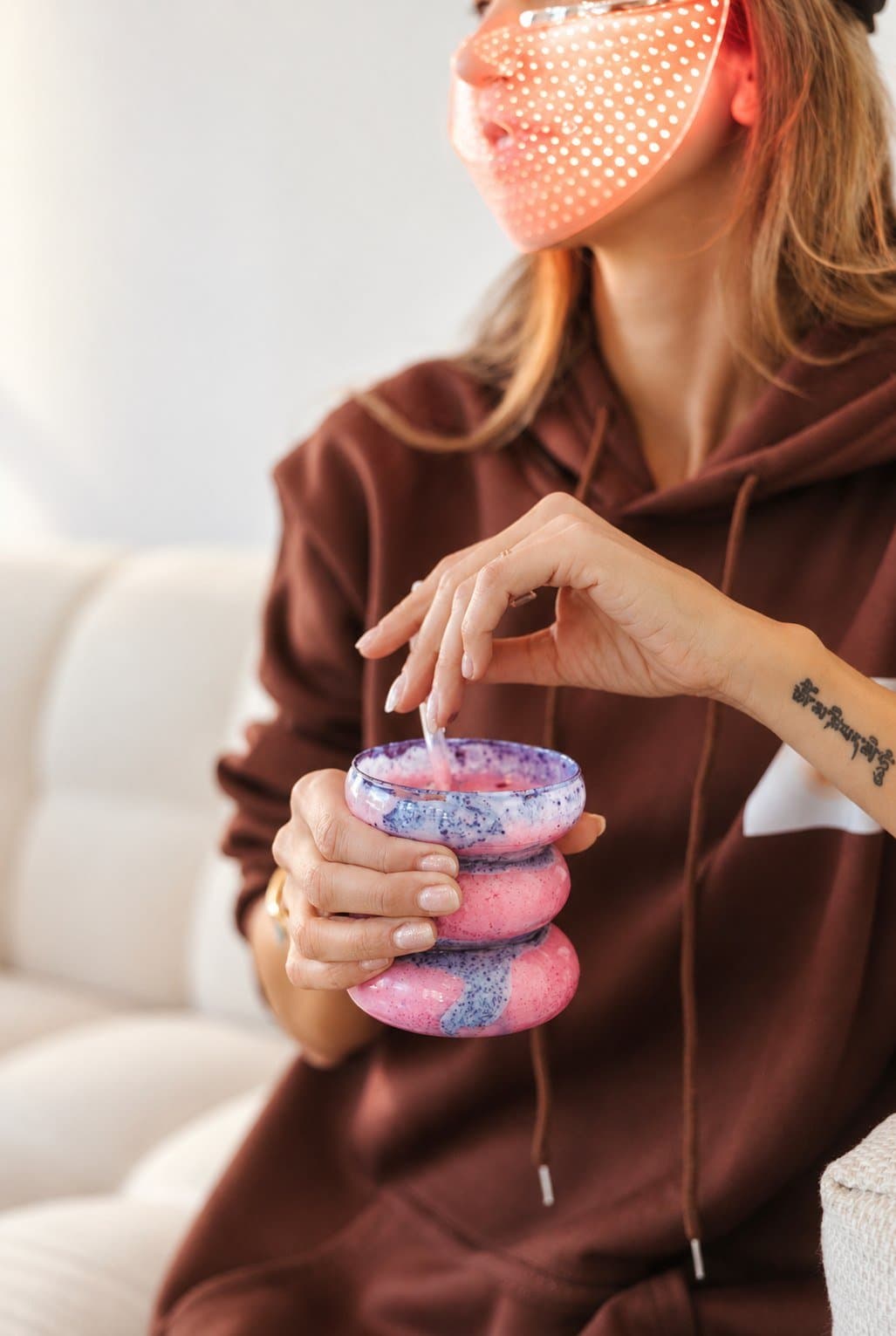 Cliente sous masque LED rouge, une boisson au collagène à la main