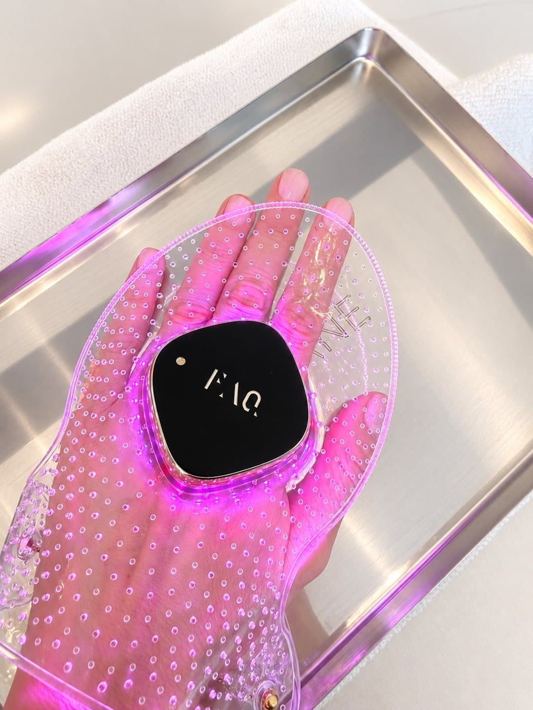 Soin LED des mains : gant lumineux rose posé sur un plateau en acier